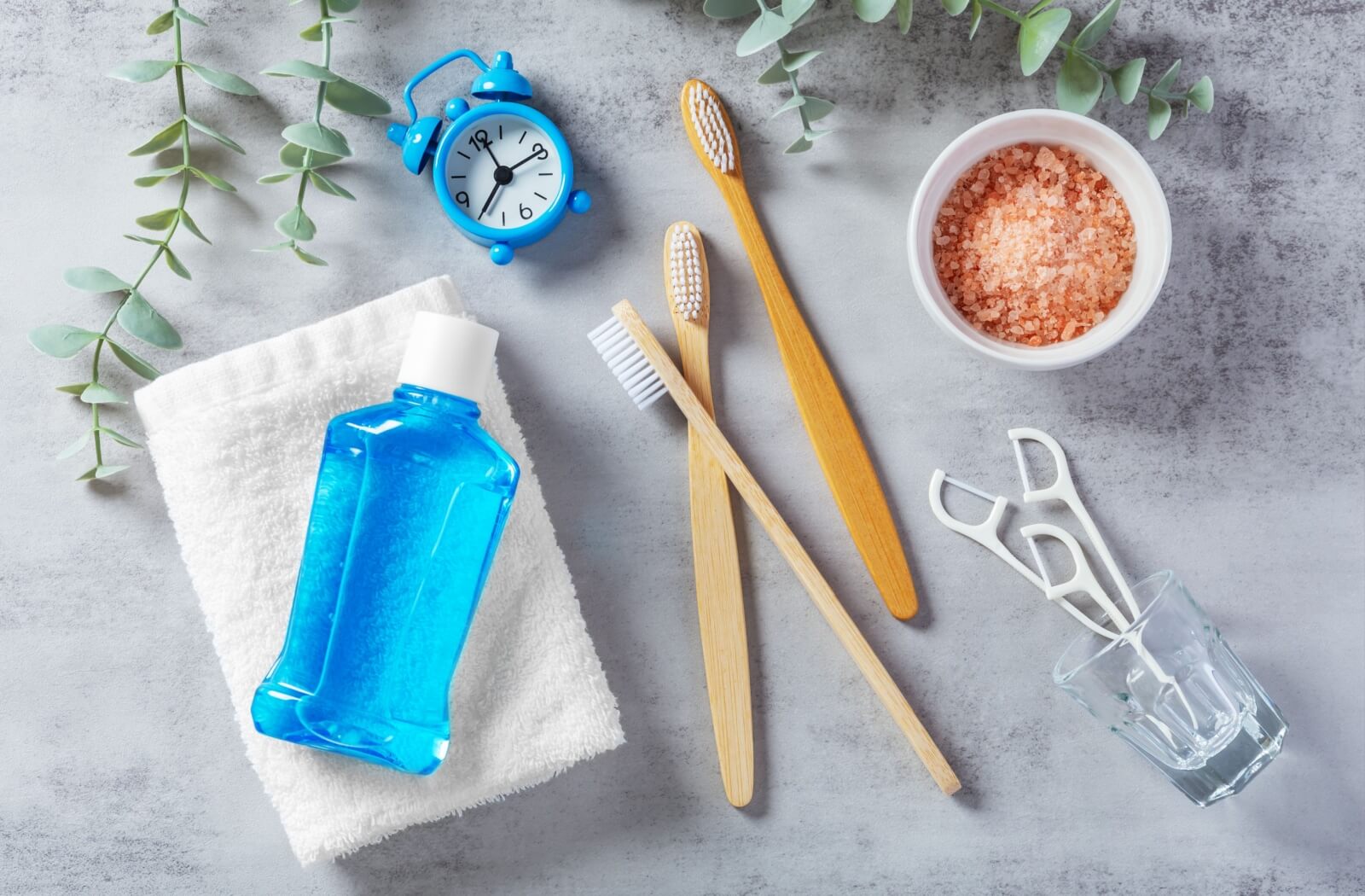 Various oral hygiene tools lay displayed on a counter, including mouthwash, toothbrushes, flossing picks and a small alarm clock.