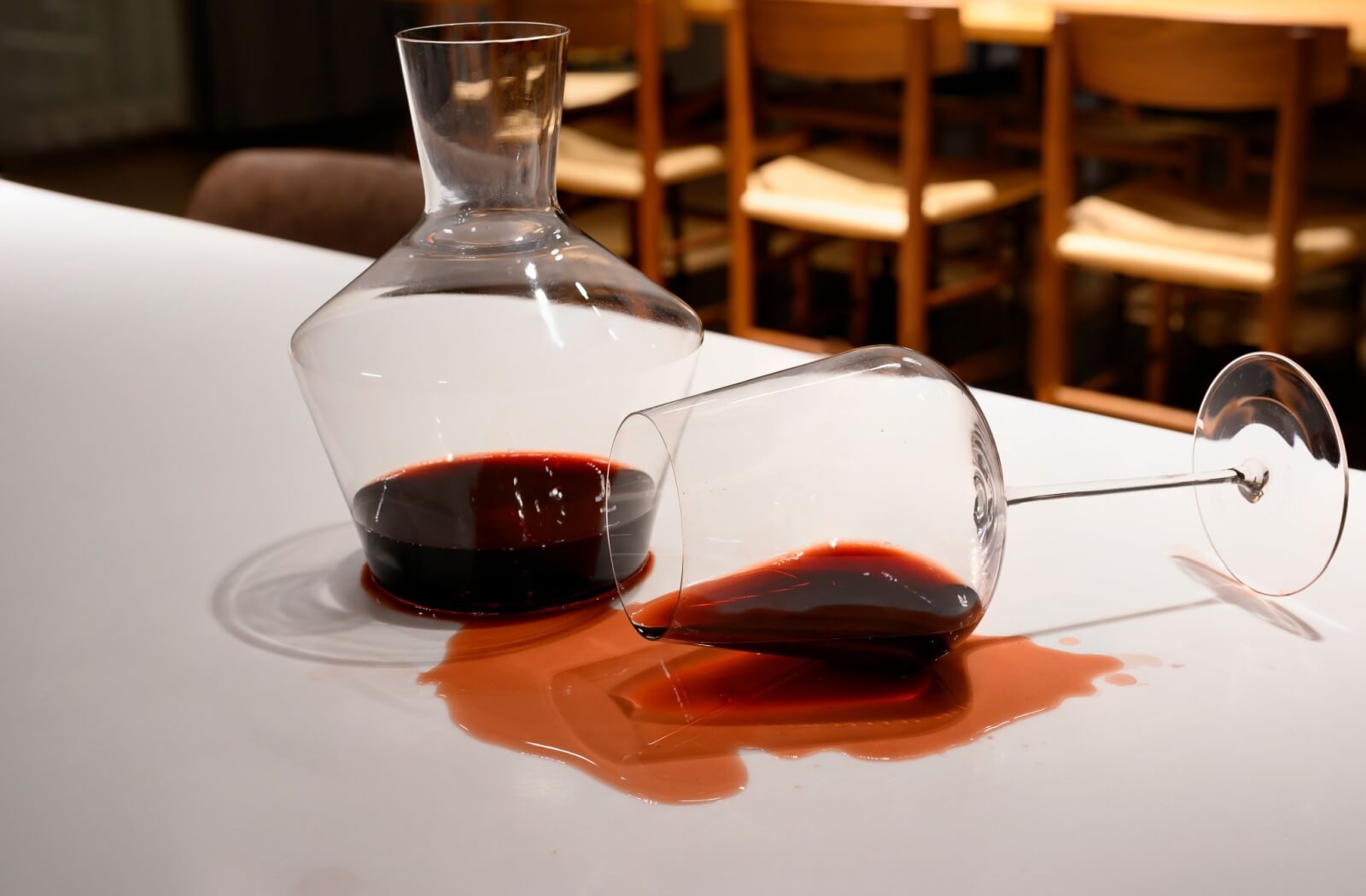 A wine glass lying on its side, spilling wine onto a stained white tablecloth.